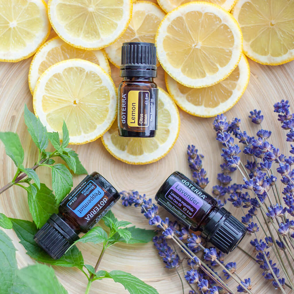 Essential oils bottles labeled lemon, lavender, and peppermint surrounded by lemon slices, lavender sprigs, and mint leaves.
