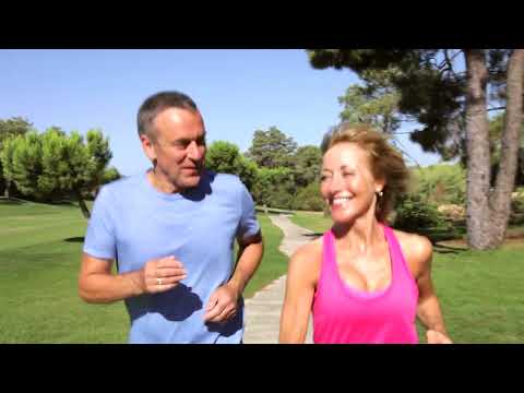 A couple in sportswear jogging outdoors on a sunny day with trees in the background.